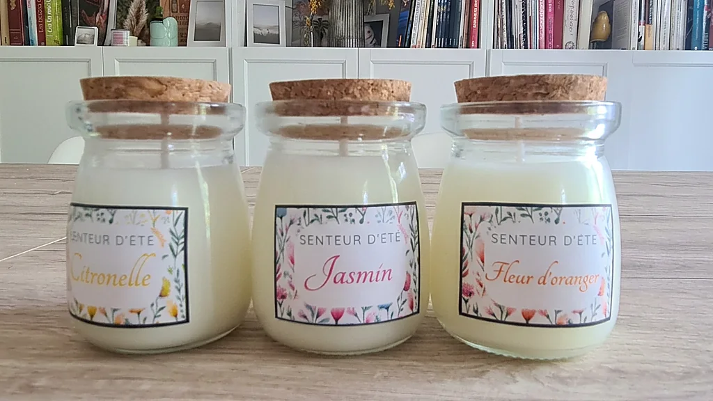 Trio de bougies parfumées senteur d'été : citronnelle, jasmin, fleur d'oranger, posées devant une bibliothèque